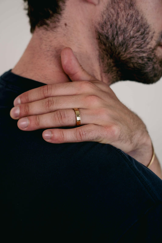 EXCITÀRE Brand Ring gold, worn on the right hand, close-up of fingers resting on opposite shoulder.
