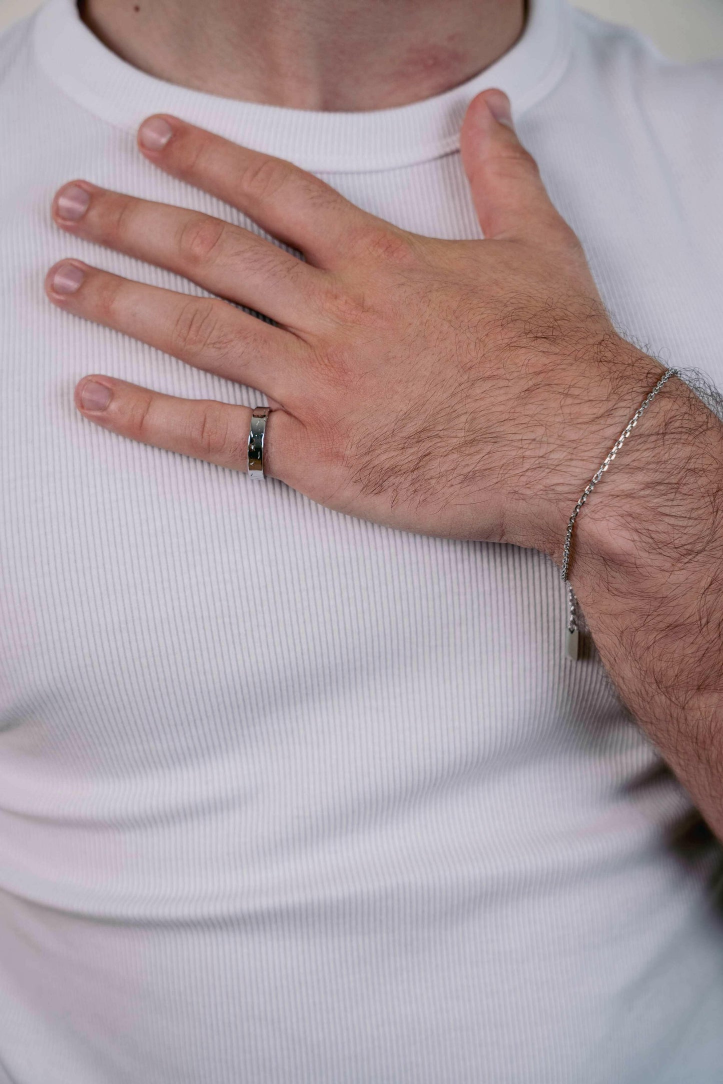 EXCITÀRE Brand Ring silver, worn on right hand, fingers spread gently across chest over a white shirt.