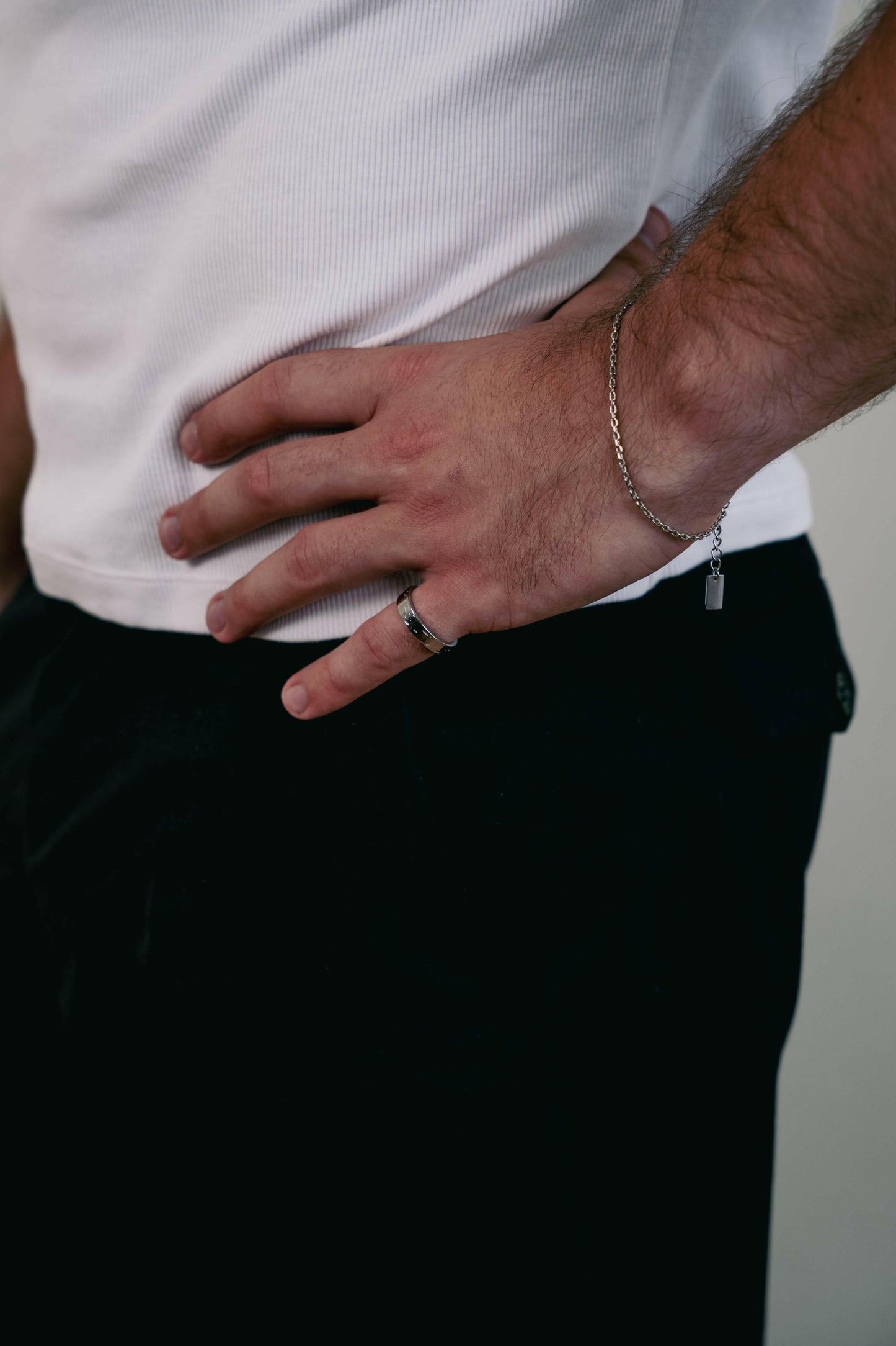 EXCITÀRE Brand Ring silver, worn on right hand, resting on hip over black trousers and white ribbed shirt.