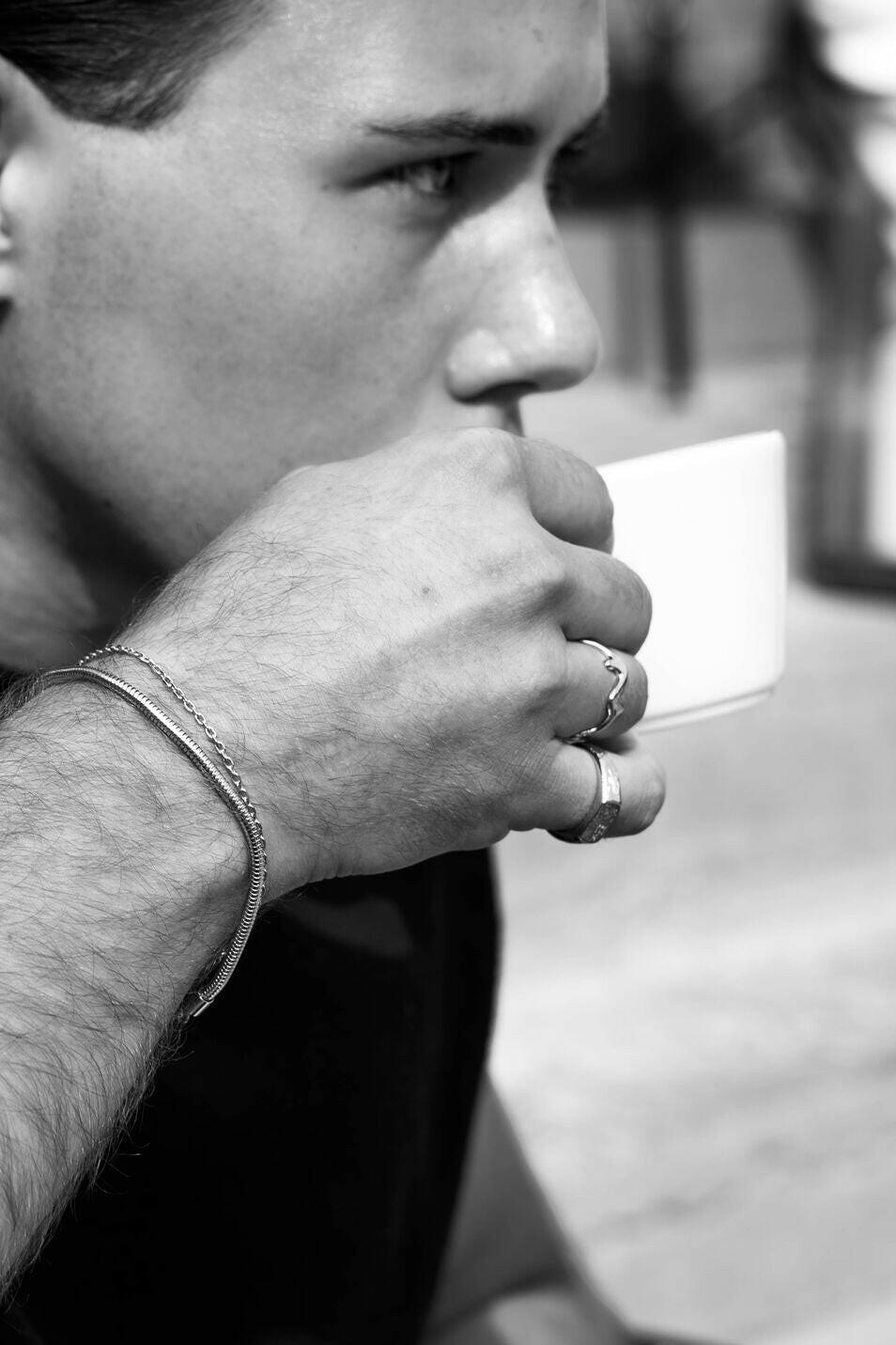 Close-up of the EXCITÀRE Ring silver paired with layered silver bracelets and another ring, worn while casually enjoying a coffee.