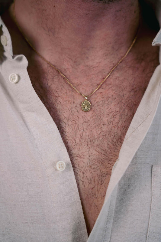 EXCITÀRE Eclipse Necklace gold with oval floral pendant, styled with open beige shirt.