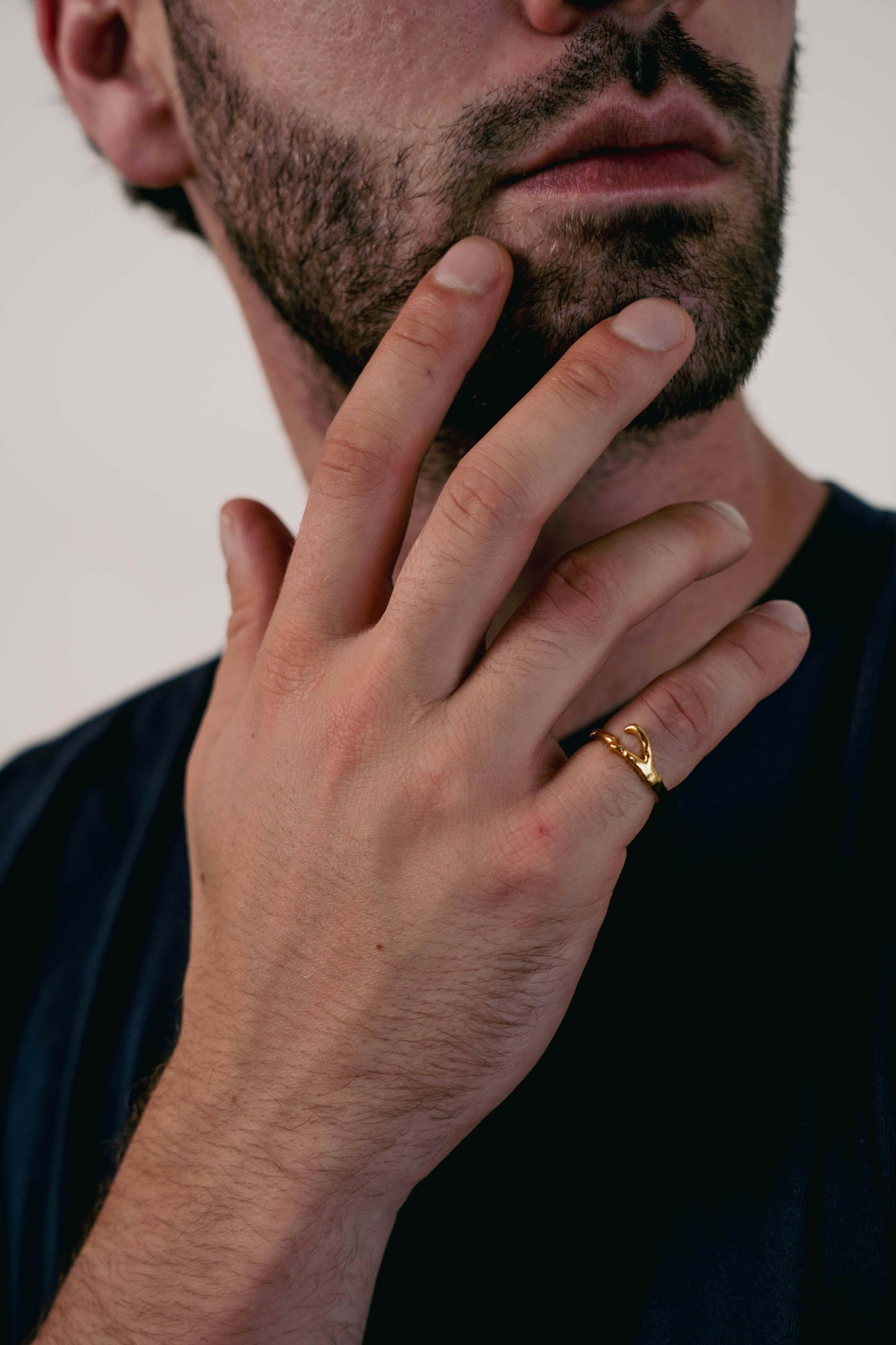 EXCITÀRE Ellis Ring gold, worn on the ring finger, hand gently touching beard in a close-up portrait.