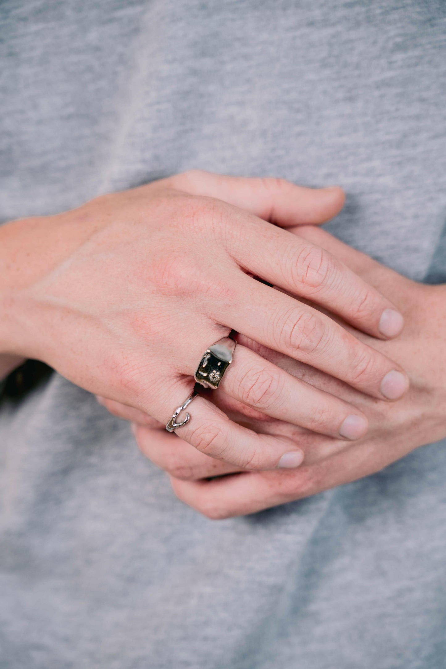 EXCITÀRE Ellis Ring silver and EXCITÀRE Ring silver worn on left hand, fingers interlocked, model in grey shirt.