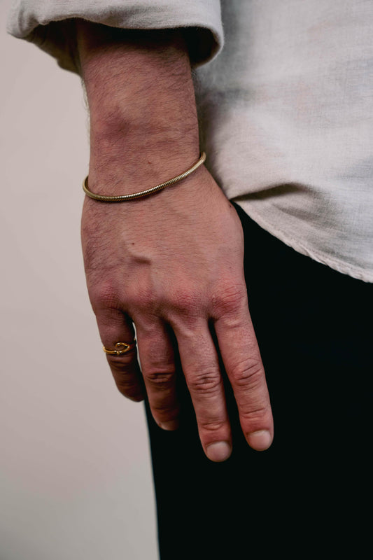 EXCITÀRE Figaro Bracelet gold with sleek chain design, styled with gold ring and light linen shirt.