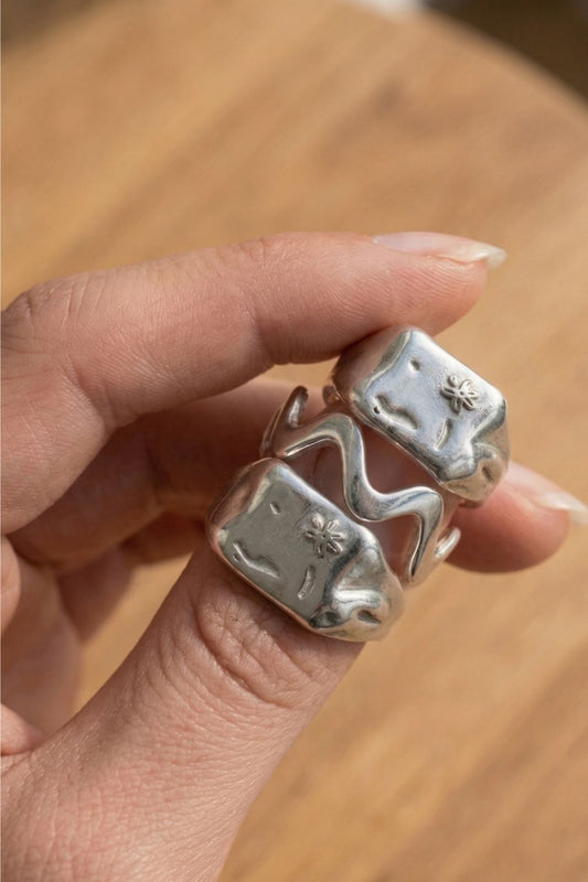 Silver ring stack with unique design held by a female hand on a wooden surface