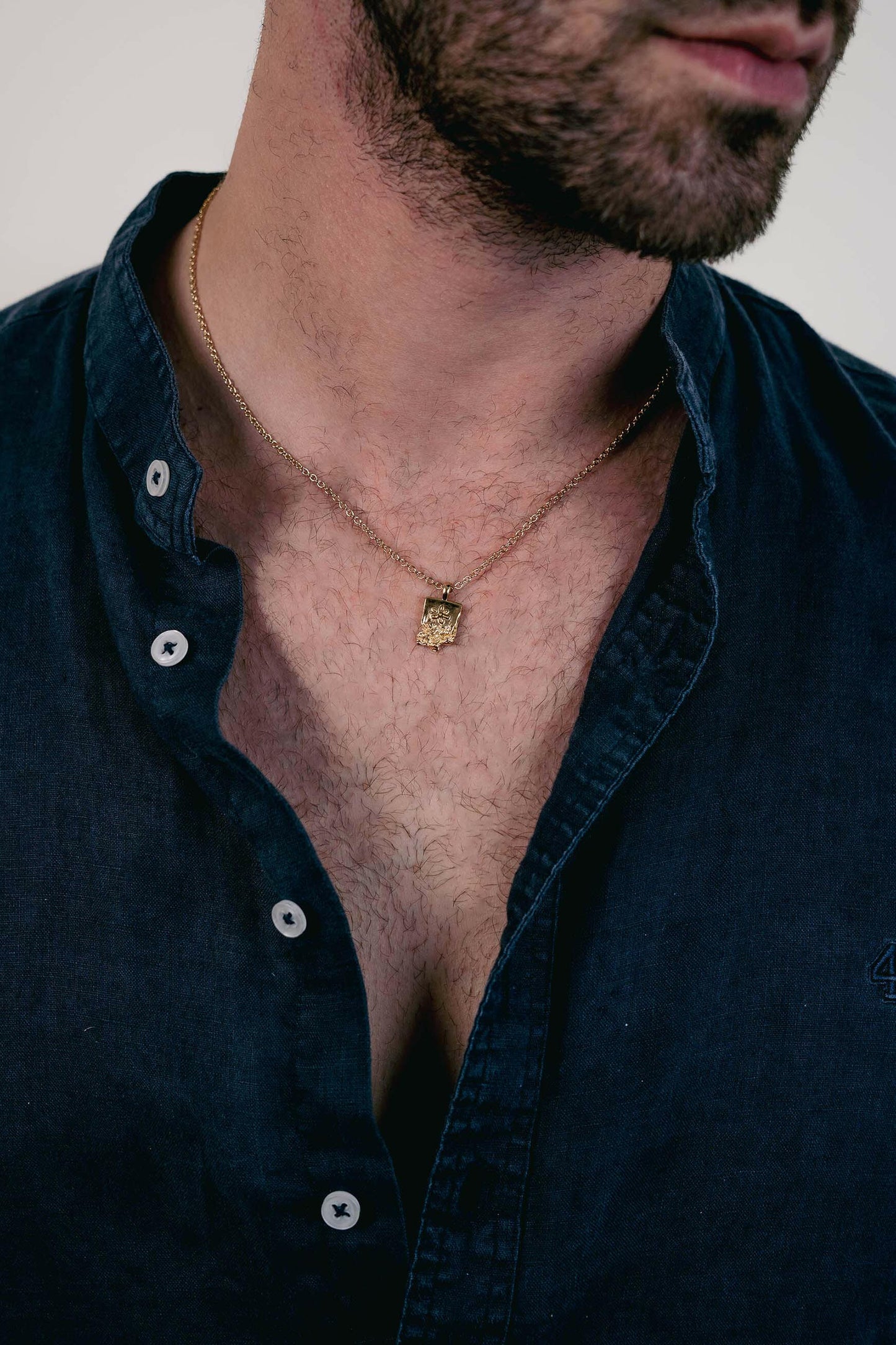 EXCITÀRE Flower Necklace gold with floral pendant, styled with open navy shirt.