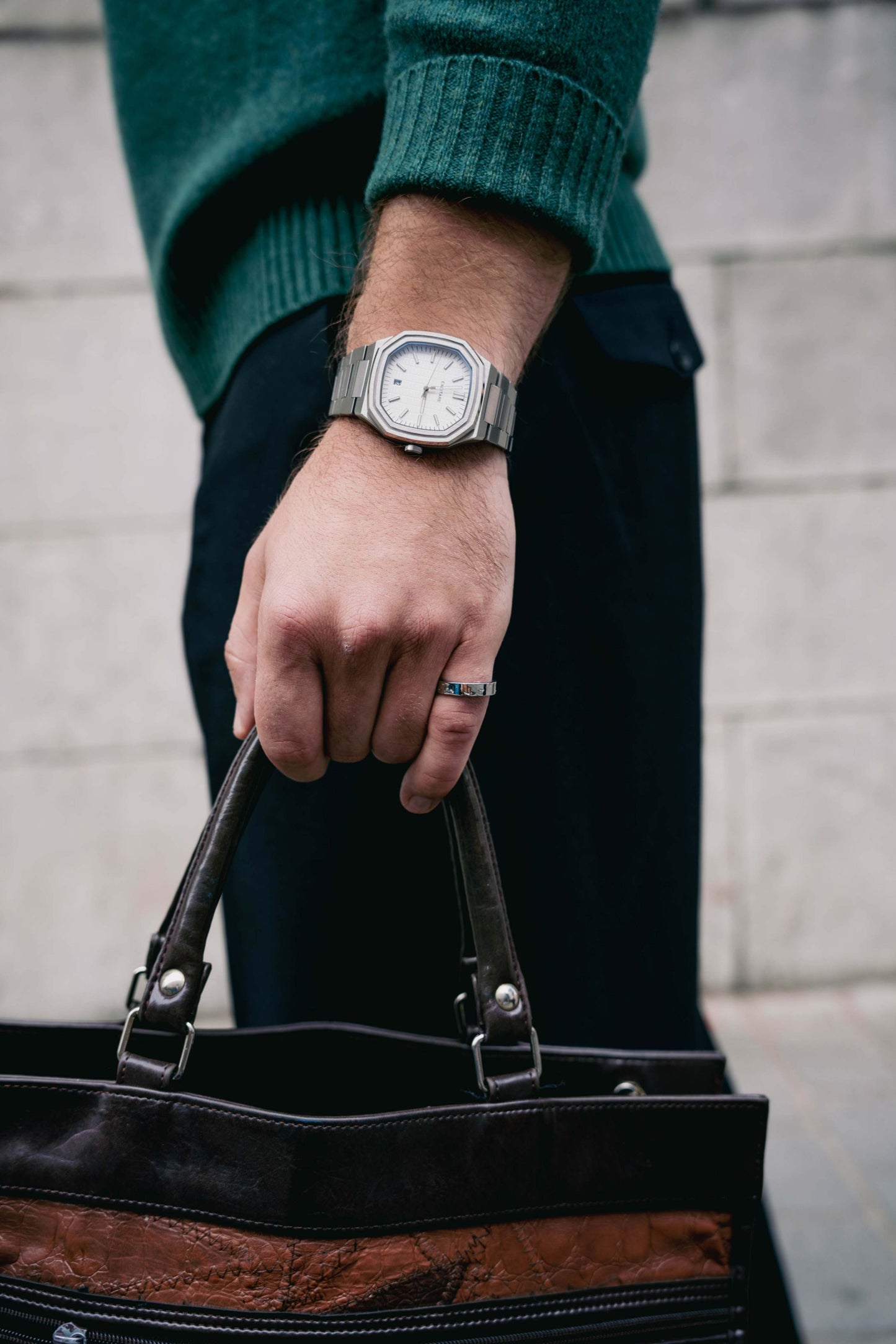 Close-up of a man's wrist wearing the Lumen White EXCITÀRE Watch with a silver metal strap, holding a dark leather bag.