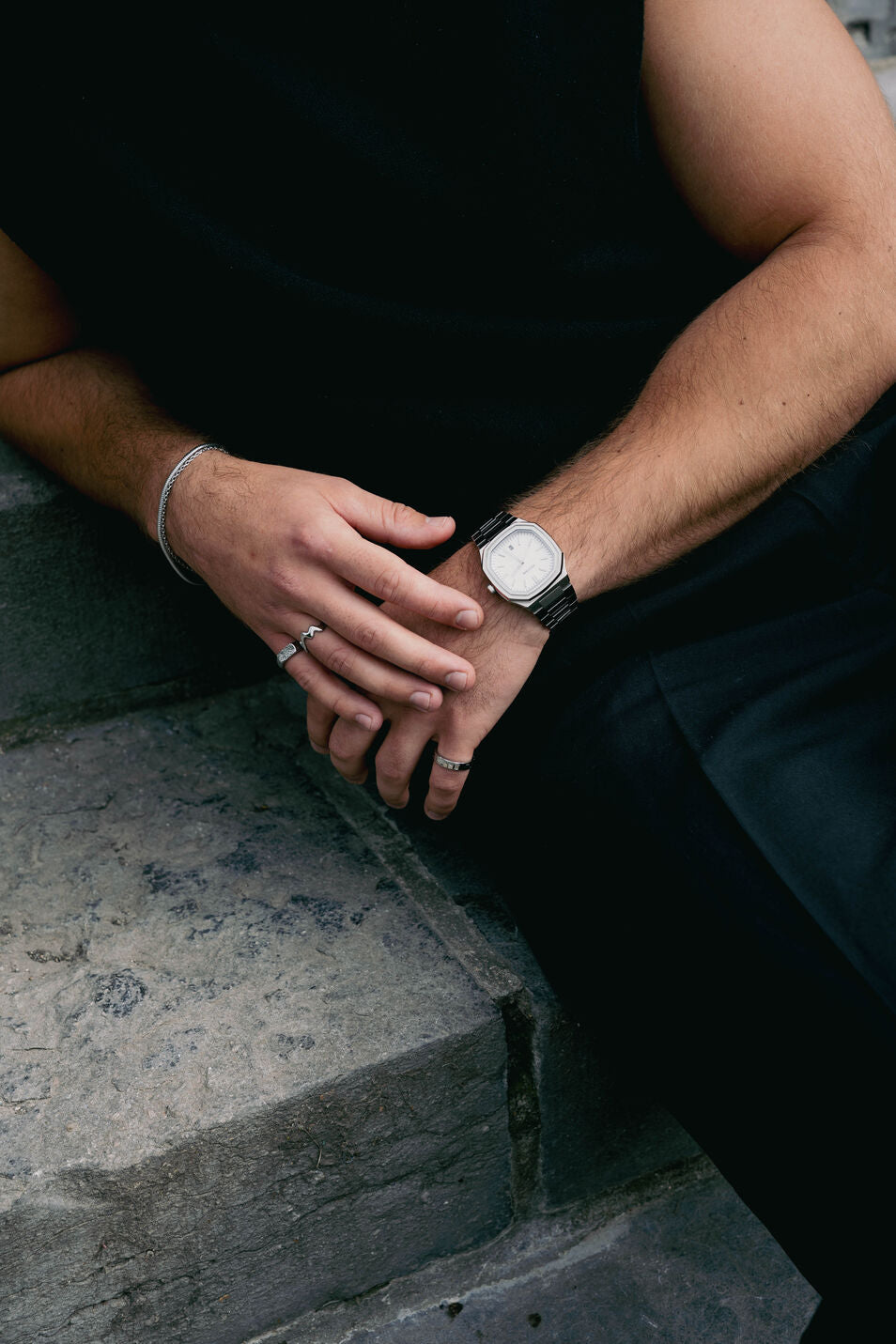 EXCITÀRE Nova Bracelet silver styled with silver rings and watch, seated on stone steps.