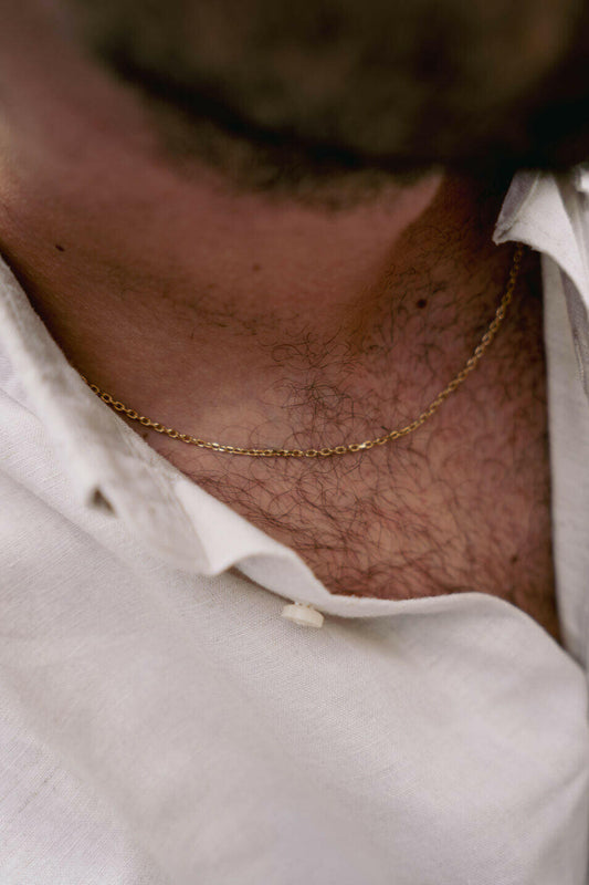 EXCITÀRE Nova Necklace gold, worn around the neck, partially visible beneath an open cream linen shirt, close-up of collarbone and chain.