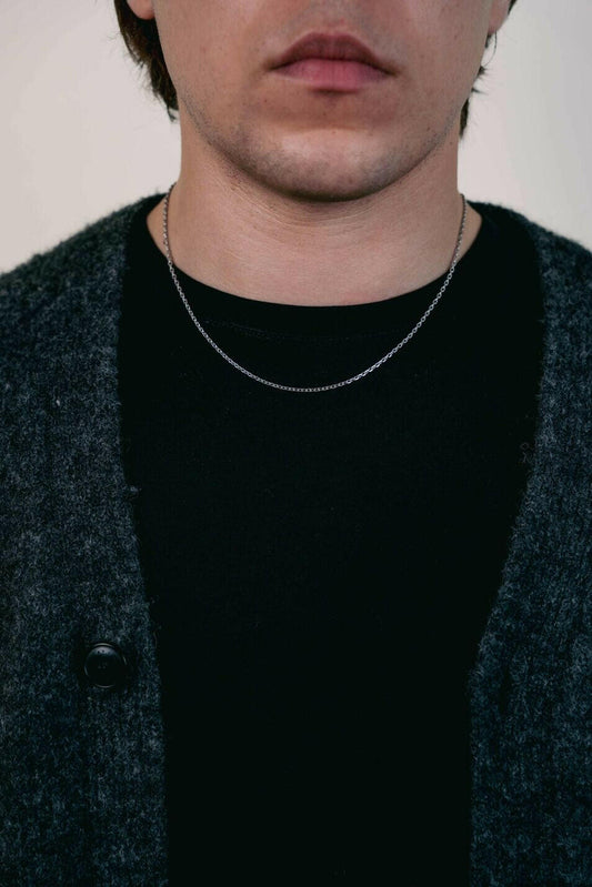 EXCITÀRE Nova Bracelet silver, worn around the neck over a black shirt and dark cardigan, shown in close-up frontal view.