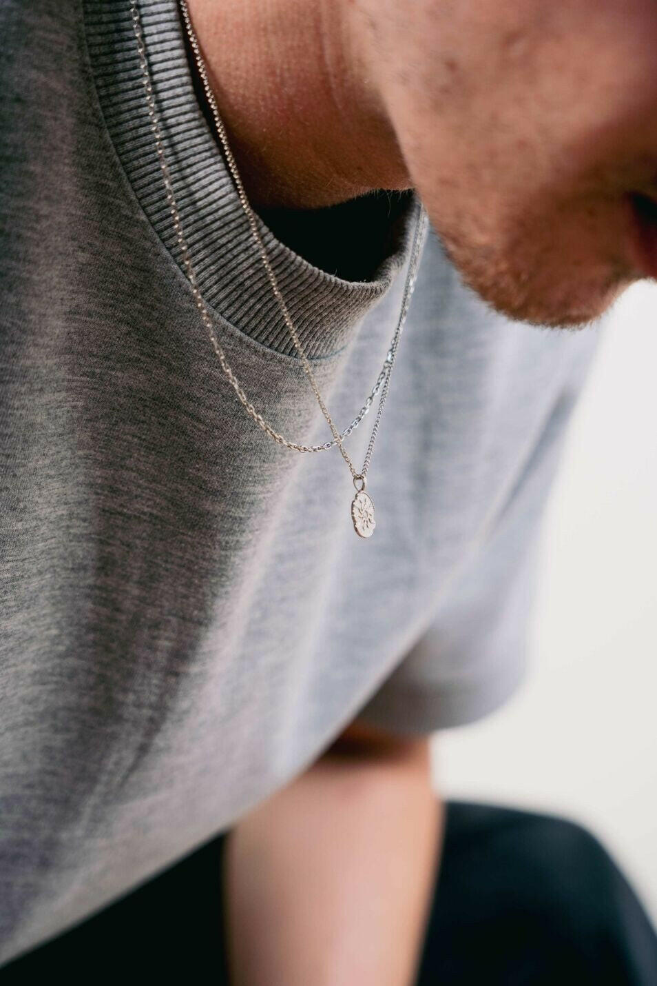 EXCITÀRE Flower Necklace silver, worn layered with a fine chain over a grey crewneck shirt, captured in a close-up side angle.