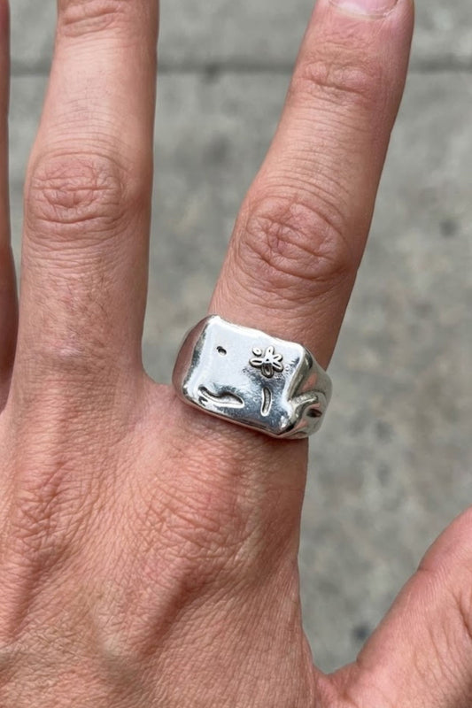 Close-up top view of the Flower Ring Extra in silver, featuring a subtle engraved flower detail on a bold minimalist signet ring, worn on the hand.