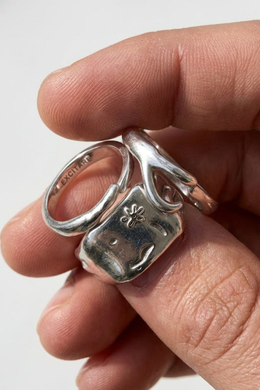 Close-up of the Flower Ring Stack Extra in silver, showing layered minimalist rings with engraved flower details, worn together on the hand.