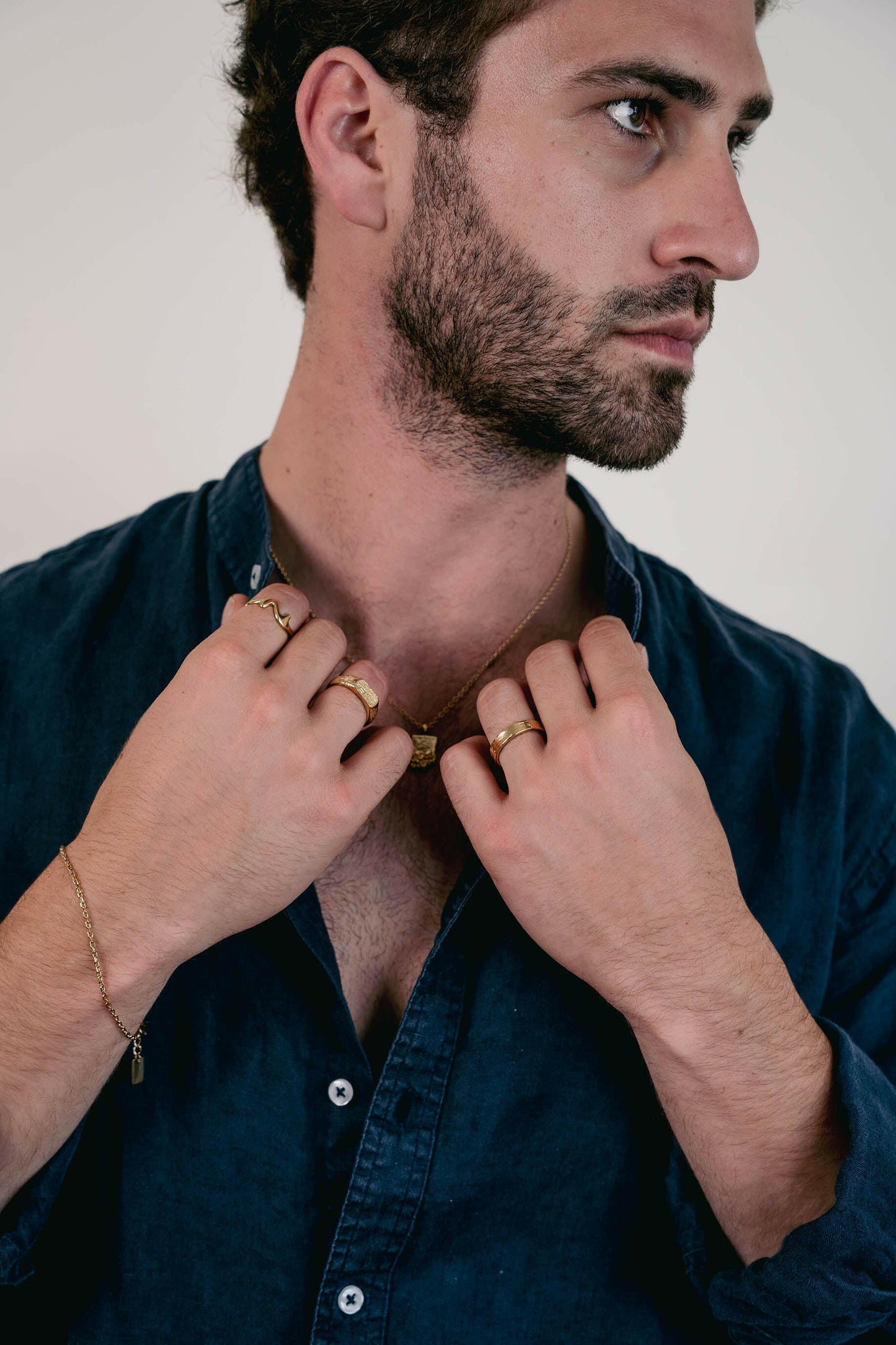 EXCITÀRE Brand Ring gold, worn on right hand, model holds necklace with both hands, looking sideways in a dark shirt.