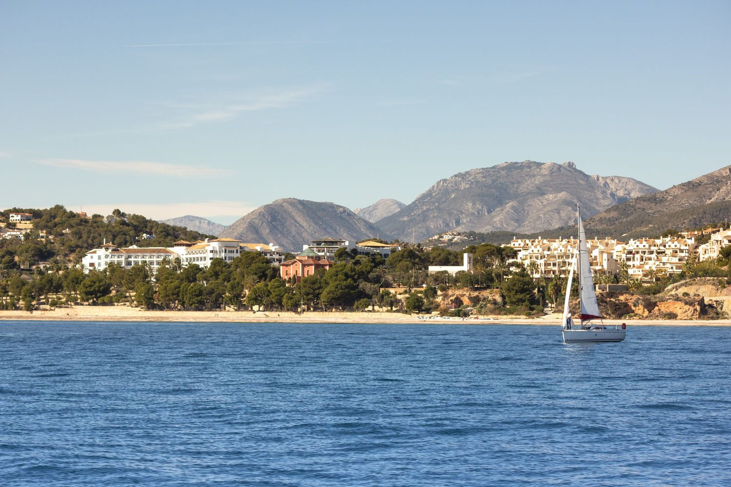 Sailboat on a blue sea with mountains and buildings in the background