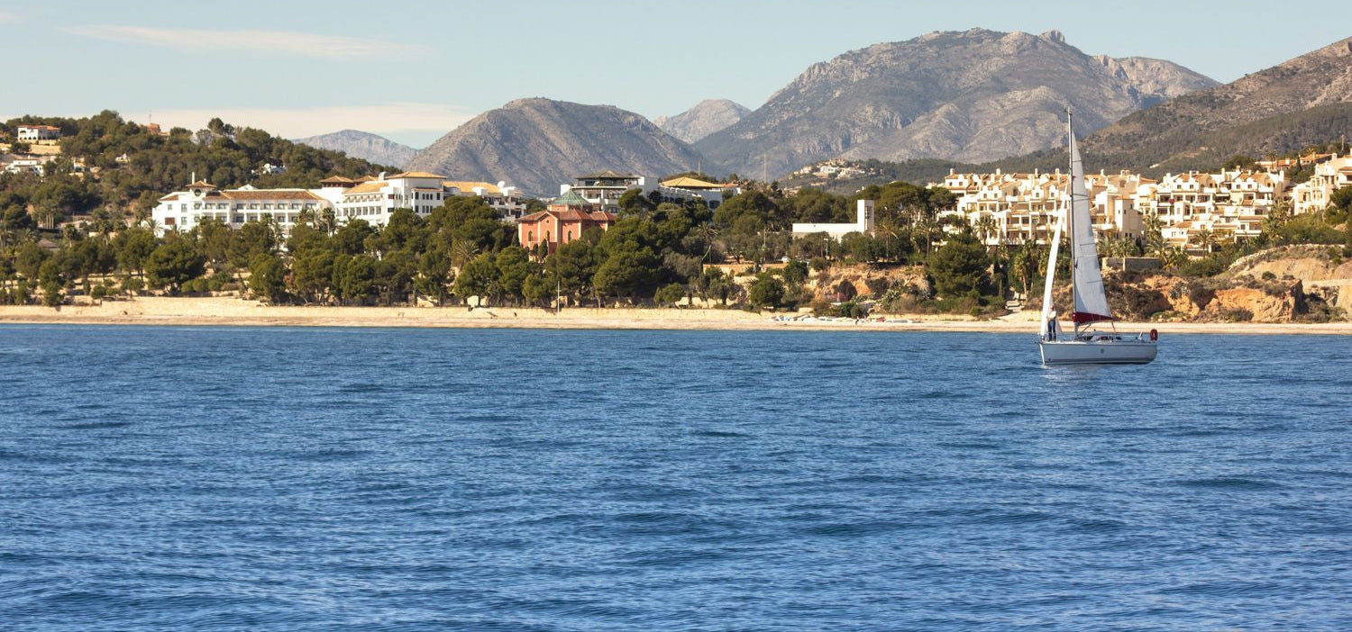 Sailboat on a blue sea with mountains and buildings in the background