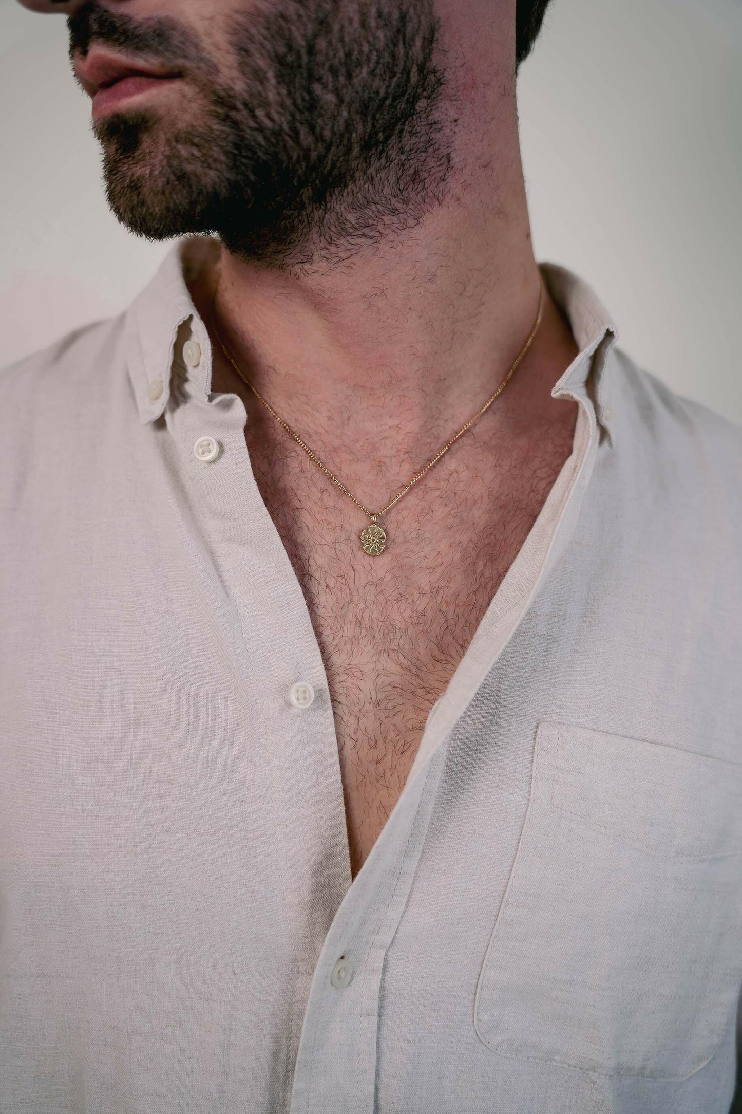 EXCITÀRE Eclipse Necklace gold with oval floral pendant, styled with open light linen shirt.