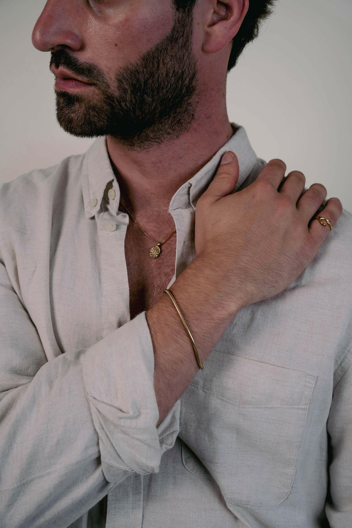 EXCITÀRE Eclipse Necklace gold with oval floral pendant, styled with gold bracelet and ring over light linen shirt.