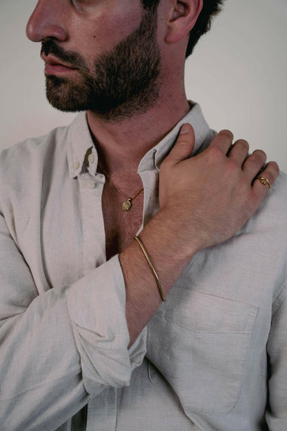 EXCITÀRE Eclipse Necklace gold with oval floral pendant, styled with gold bracelet and ring over light linen shirt.
