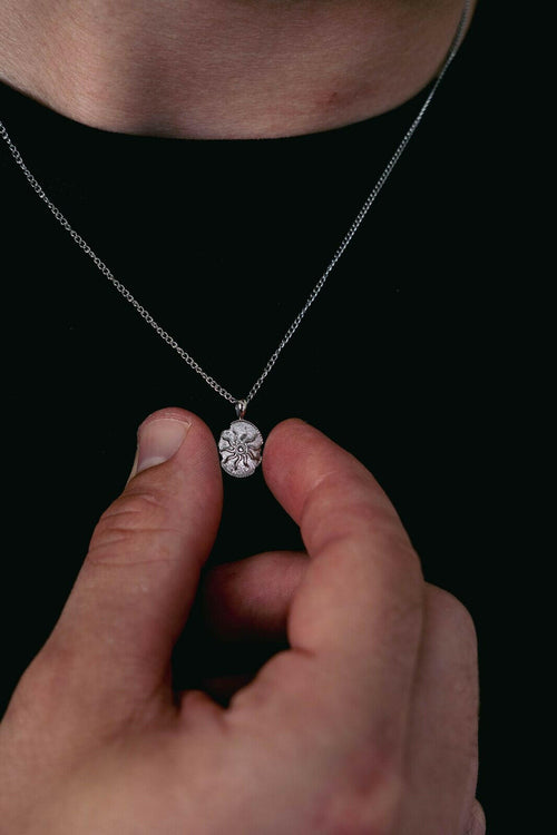 Close-up of a silver pendant necklace sitting high and visible on a black t-shirt.