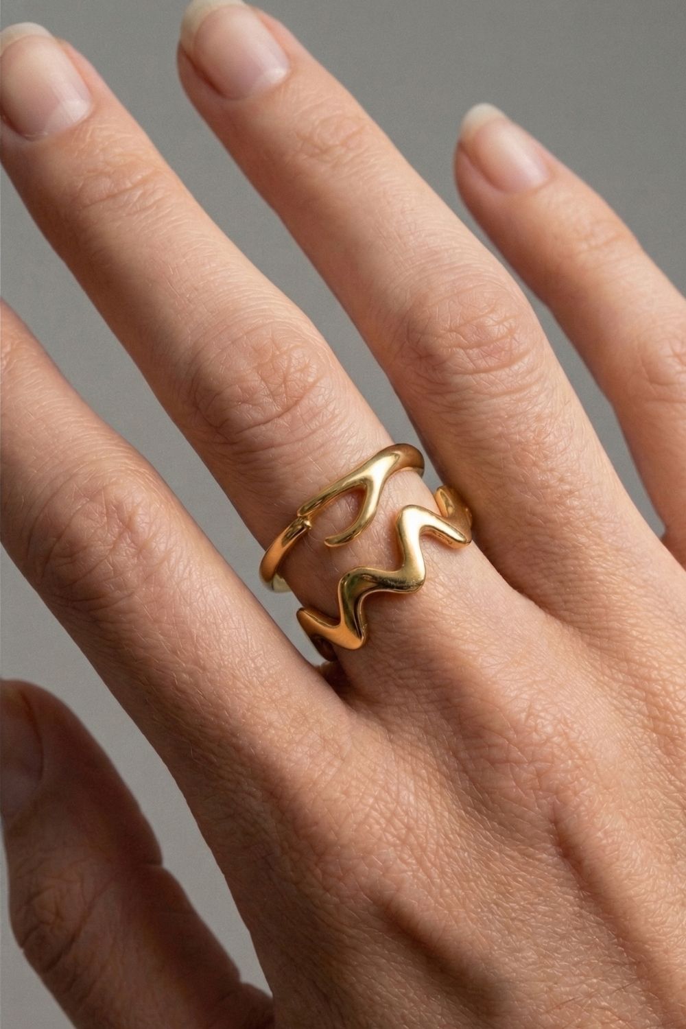 Gold ring stack on a female finger against a neutral grey background