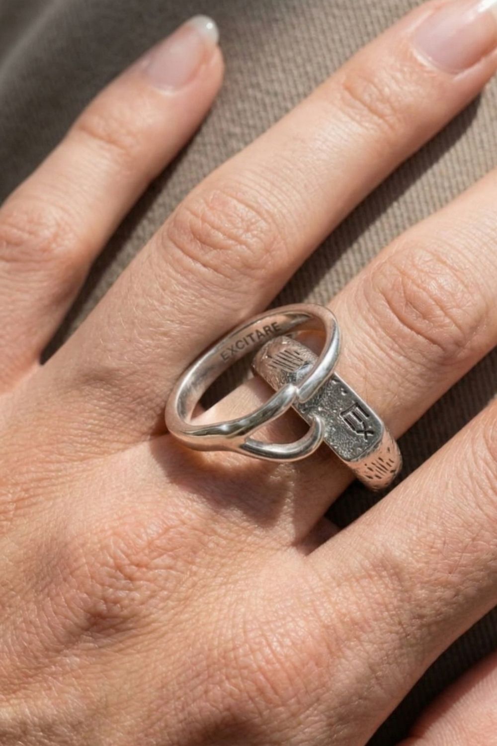 Close-up of a female hand wearing the silver EXCITARE ring with engraved design on a neutral background