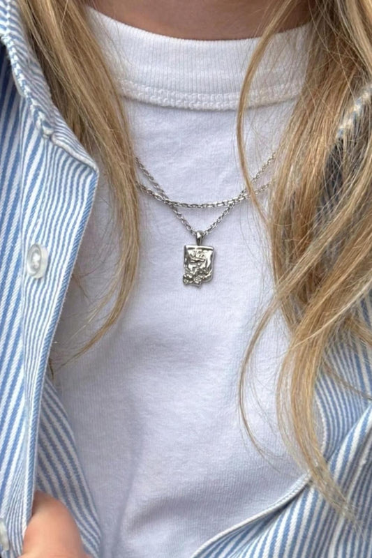 
  Female wearing the flower necklace with a pendant, dressed in a white shirt and blue striped jacket.
