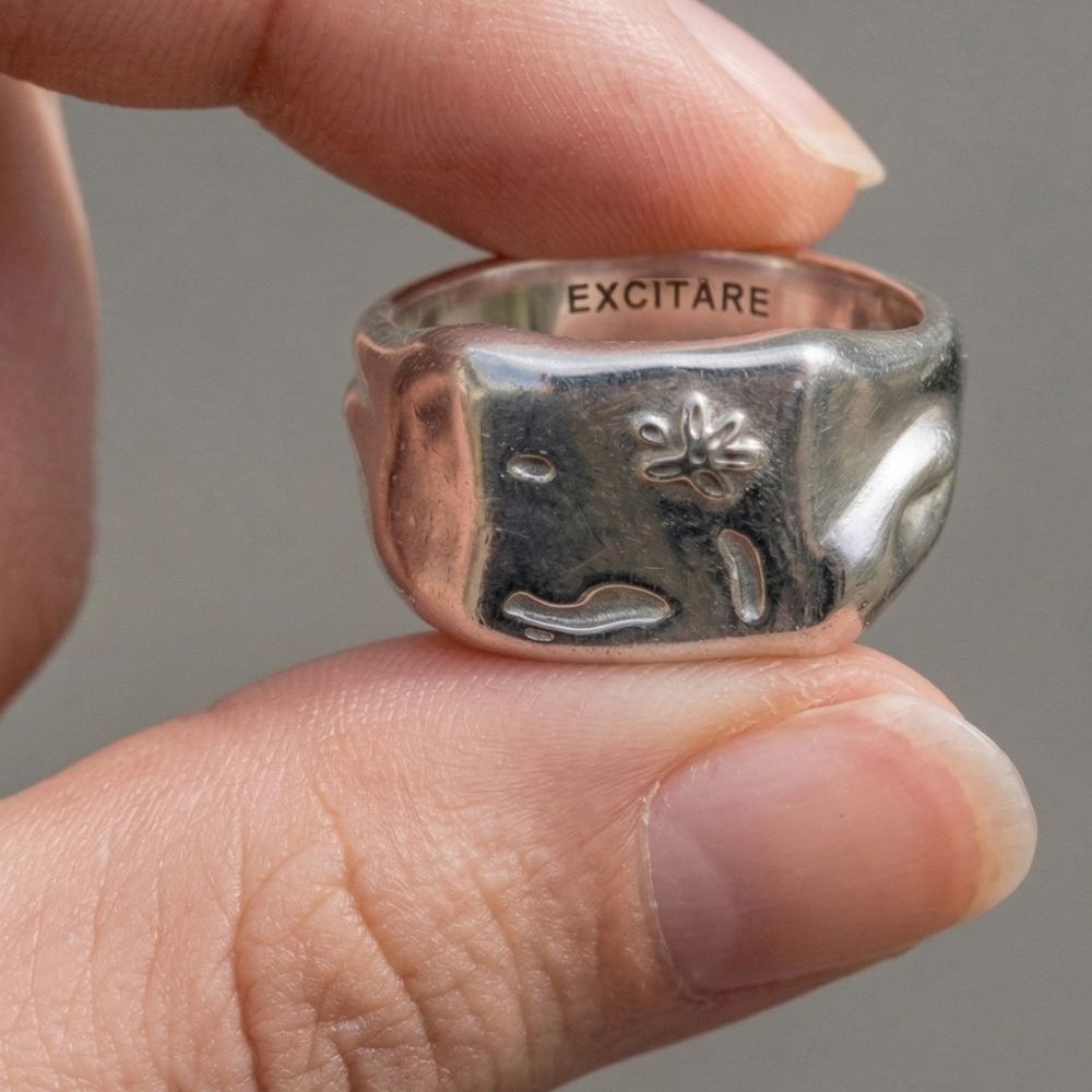 Silver ring with engraved design held between fingers against a neutral background