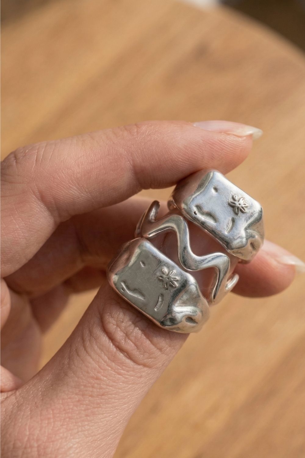 Silver ring stack with unique design held by a female hand on a wooden surface