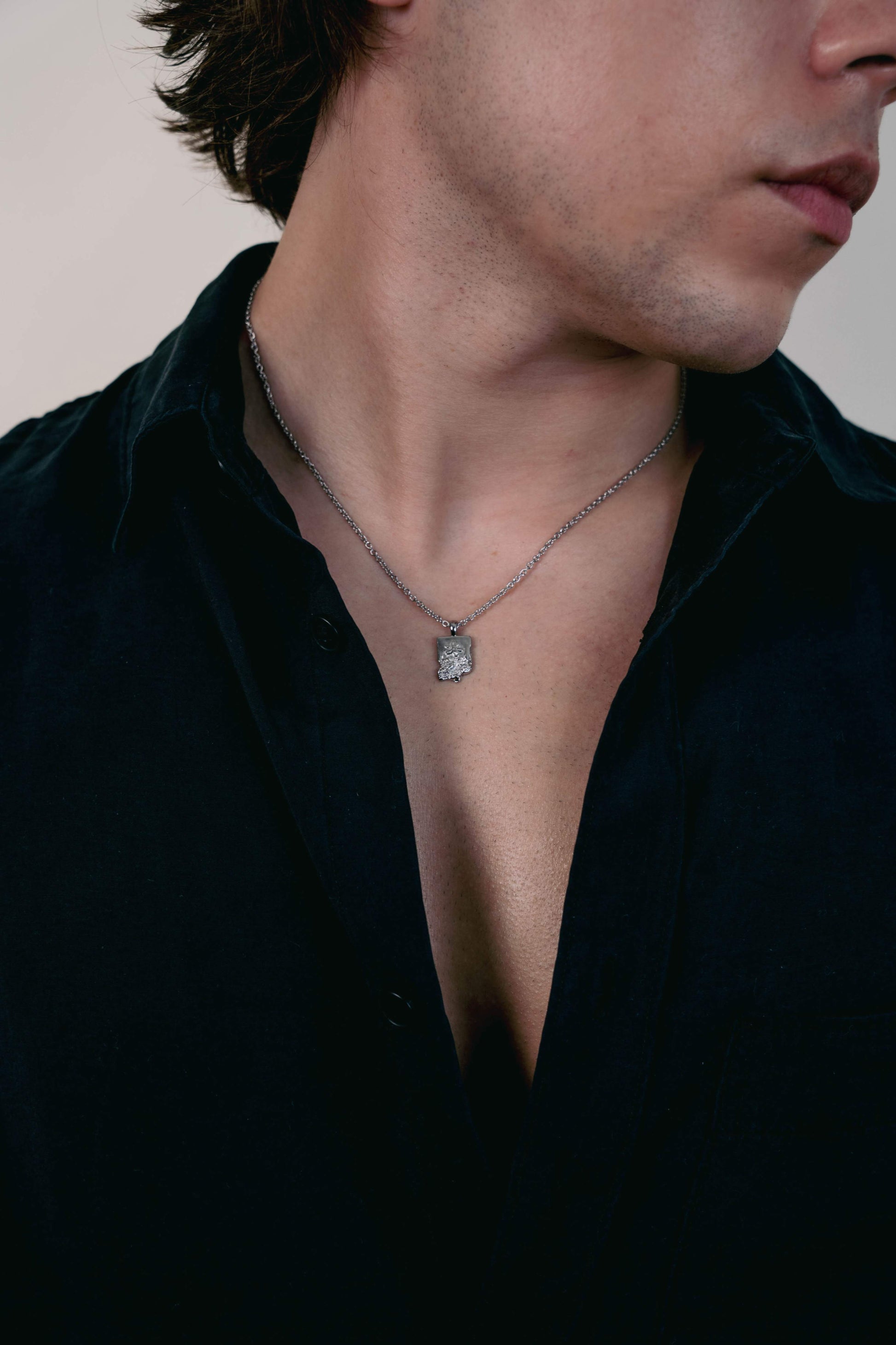 EXCITÀRE Flower Necklace silver with rugged floral pendant, worn with open black shirt.