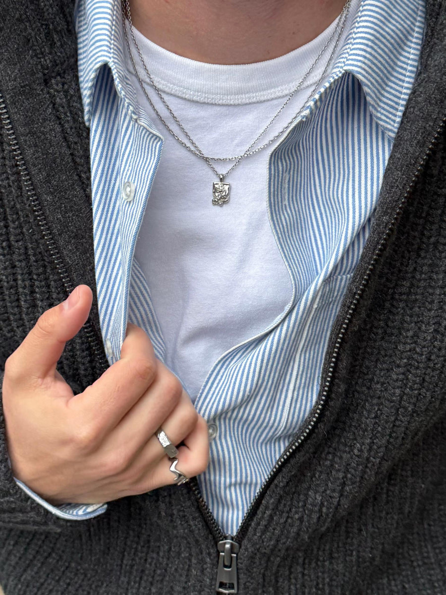 Gelaagde ketting styling met een hanger en een schoon T-shirt onder een getextureerde trui voor een streetwear look