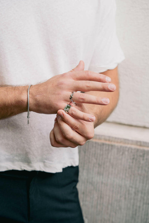Hand wearing a silver ring styled with a white t-shirt and relaxed trousers.