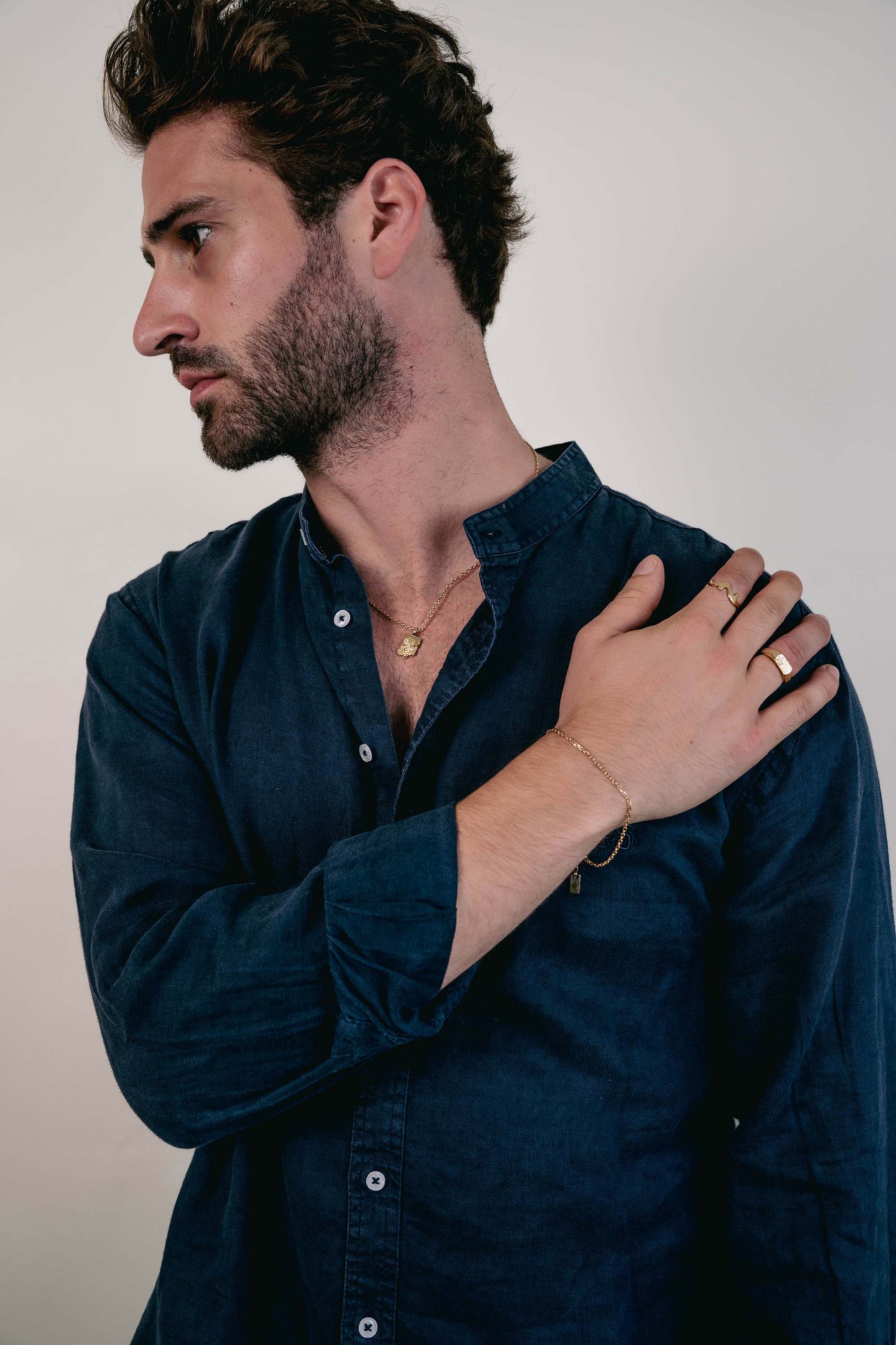 EXCITÀRE Nova Bracelet gold styled with layered gold rings from EXCITÀRE and necklace, worn with navy shirt.
