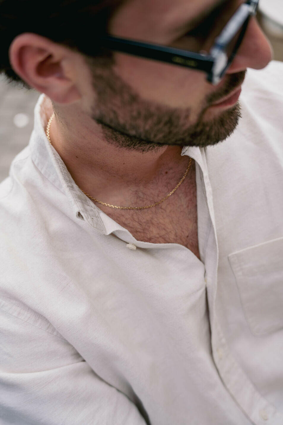 EXCITÀRE Nova Necklace gold, worn around the neck, paired with sunglasses and an open cream shirt, seated pose with head turned sideways.