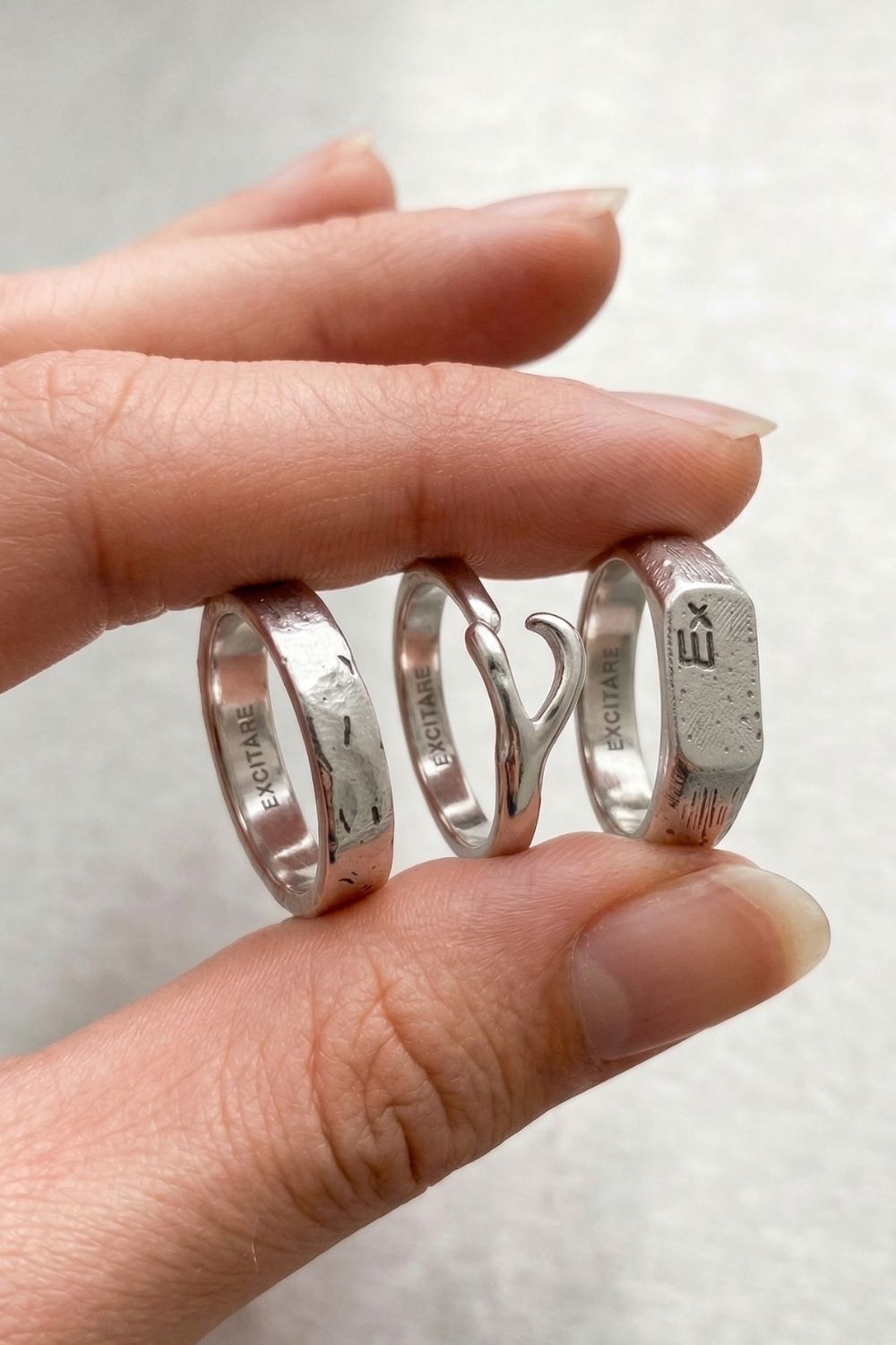 Female Hand holding three silver rings with engraved text on a light background