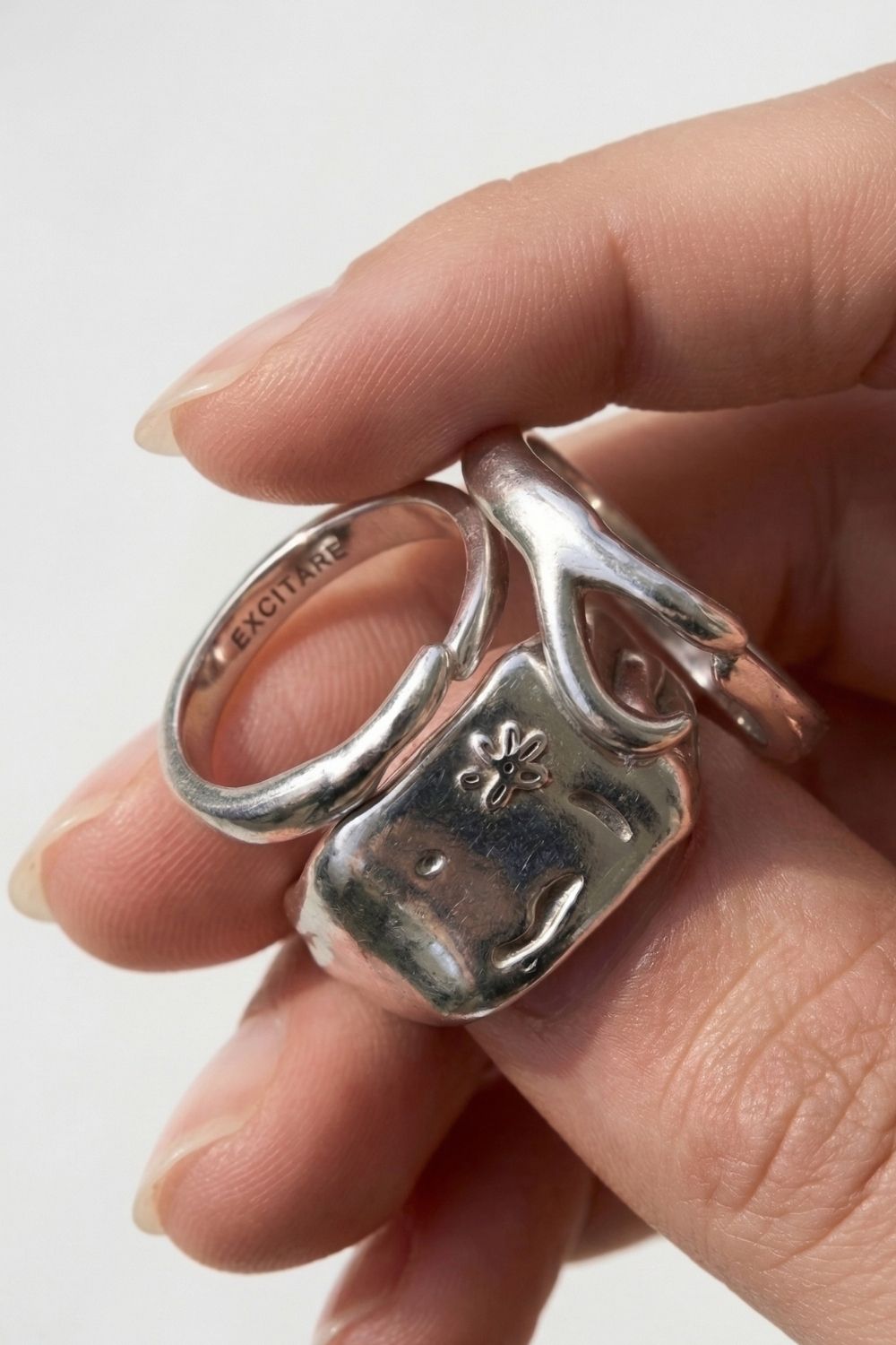 Female Hand holding two silver rings with intricate designs on a light background