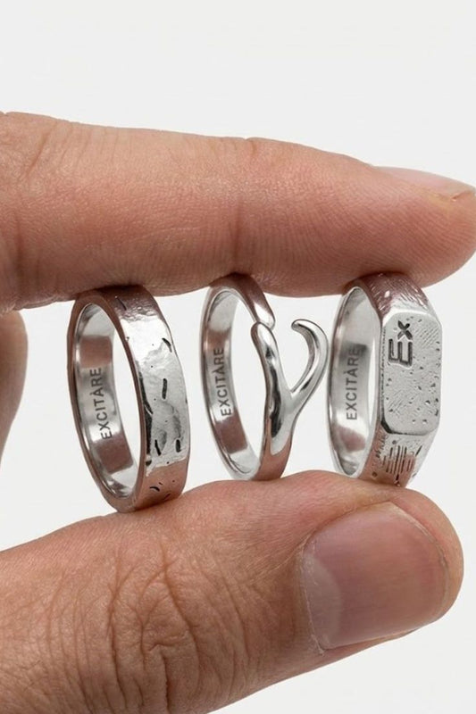 
  Top view of the Brand Ring Extra ring stack in silver, showing multiple minimalist rings with engraved EXCITARE branding, held between fingers.
