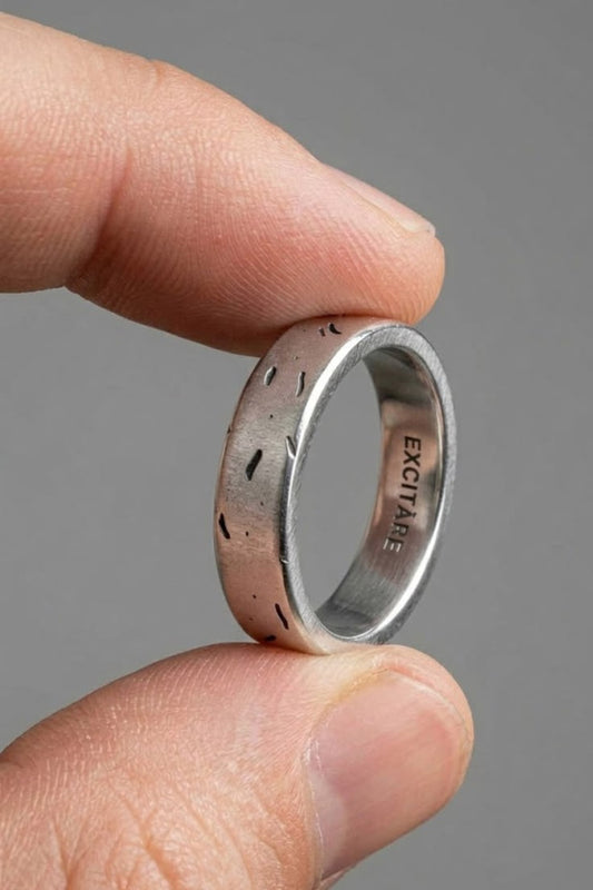 
  Silver ring with engraved design held between two fingers against a gray background
